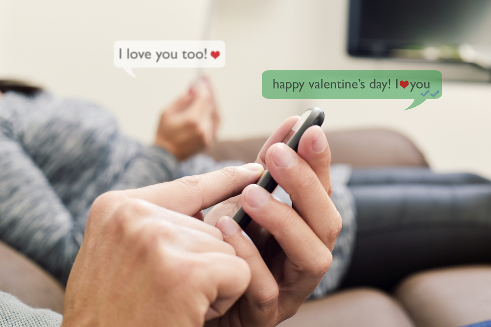 a young caucasian man and a young caucasian woman sending and receiving text messages in their smartphones with the text Happy valentines day, I love you and I love you too